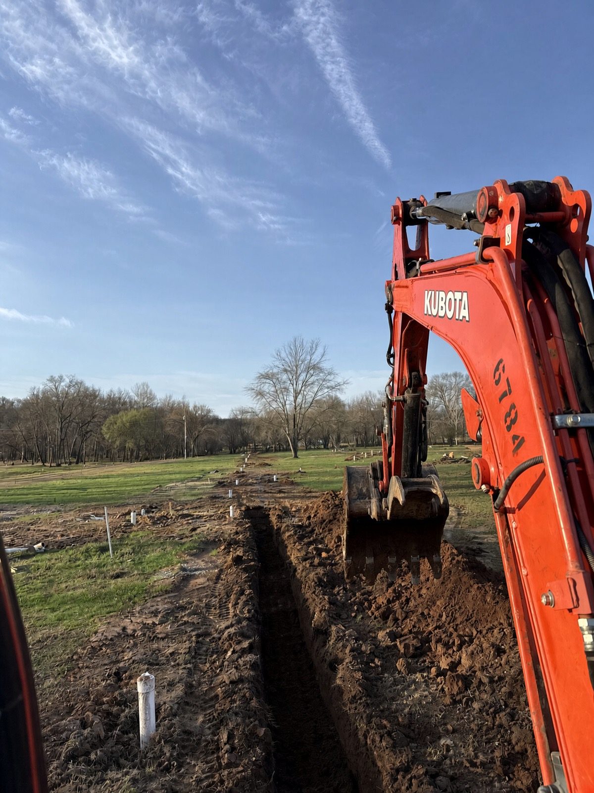 Kubota excavator working an open trench with stakes along the line